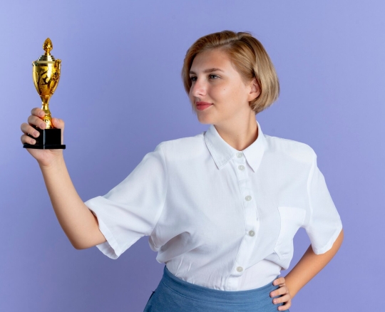 young-confident-blonde-russian-girl-holds-looks-winner-cup-isolated-purple-background-with-copy-space_141793-65185